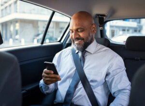 Business traveler enjoying comfortable Cumming limo service ride while using smartphone.